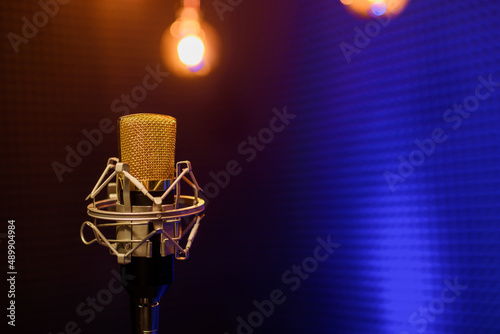 Professional microphone in a recording audio studio with acoustic panels behind it, and blue light on a background.