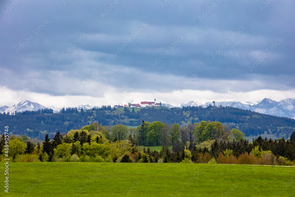 Bavarian alpine foothills landscape with green meadows forests and slightly cloudy sky.