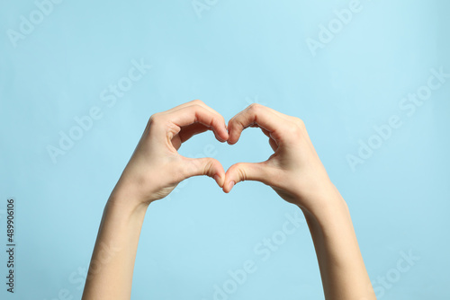 Woman making heart with her hands on light blue background  closeup