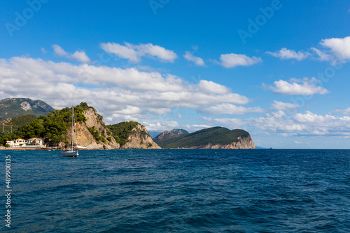 View of a sea and sailing boat with hills and blue sky with white fluffy clouds in background
