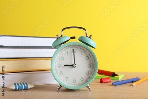 Turquoise alarm clock and different stationery on white wooden table against yellow background. School time