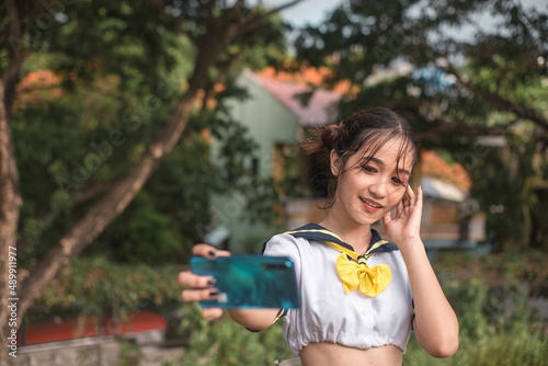 Εκτύπωση καμβά A petite young cosplayer in a sailor crop top uniform takes a selfie with her smartphone