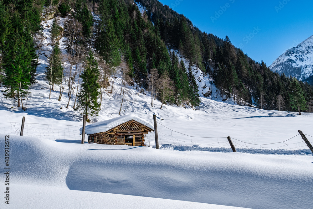 Wooden hut on a snow covered field in front of a fence in a snowy landscape with blue sky in ski resort Grossarlberg Salzburg Austria