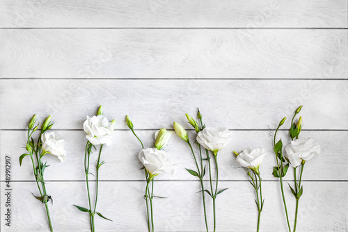 A white wooden background and white flowers of eustoma or lisianthus lie in a row at the bottom photo