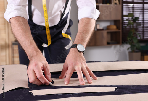 Professional tailor marking sewing pattern on fabric with chalk at table in workshop, closeup