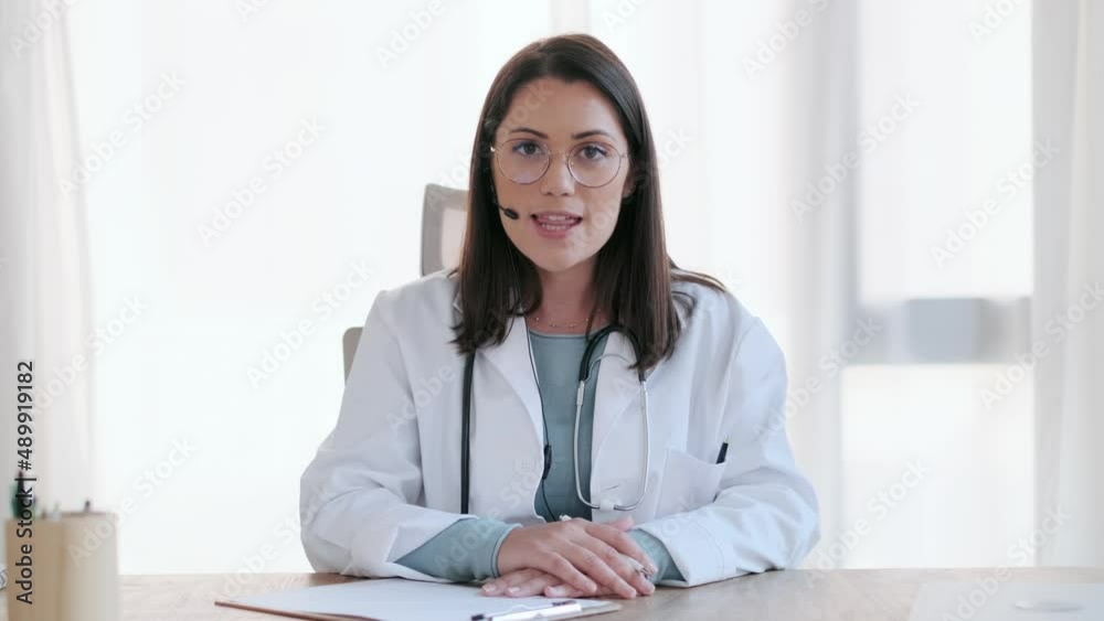 Video of female doctor talking while explaining medical treatment to patient through a video call with laptop and earphones in the consultation. Video of female doctor talking while explaining medical treatment to patient through a video call with laptop and earphones in the consultation.