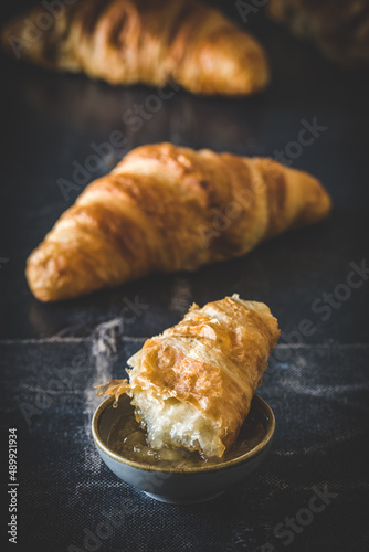 Piece of delicious French croissant dipped in jam, black background, vertical