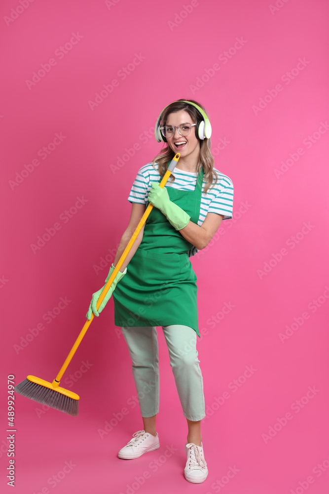 Beautiful young woman with headphones and floor brush singing on pink background Beautiful young woman with headphones and floor brush singing on pink background