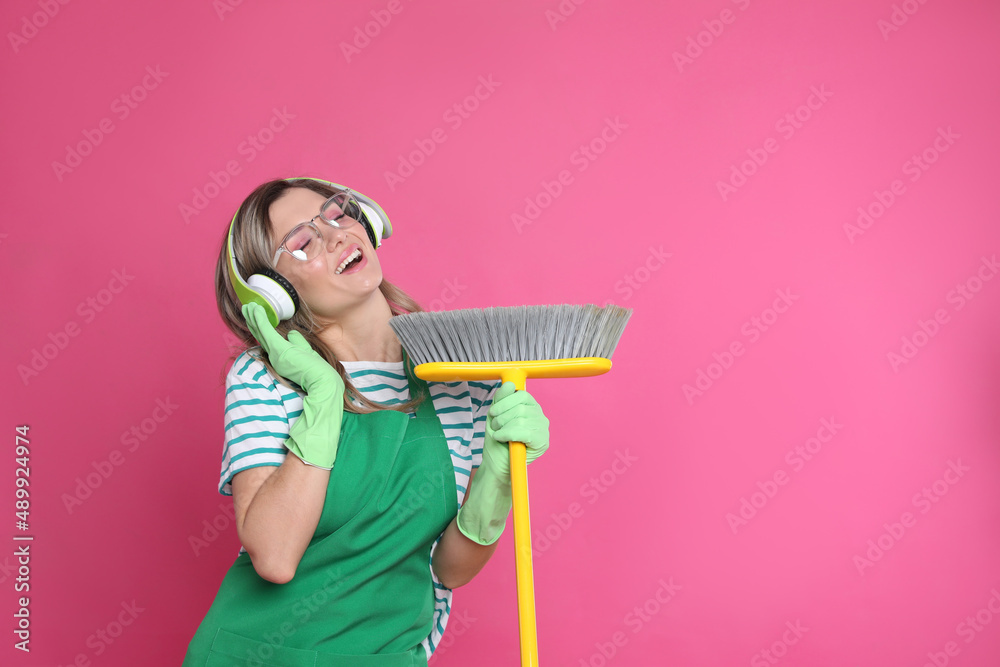 Beautiful young woman with headphones and floor brush singing on pink background. Space for text Beautiful young woman with headphones and floor brush singing on pink background. Space for text