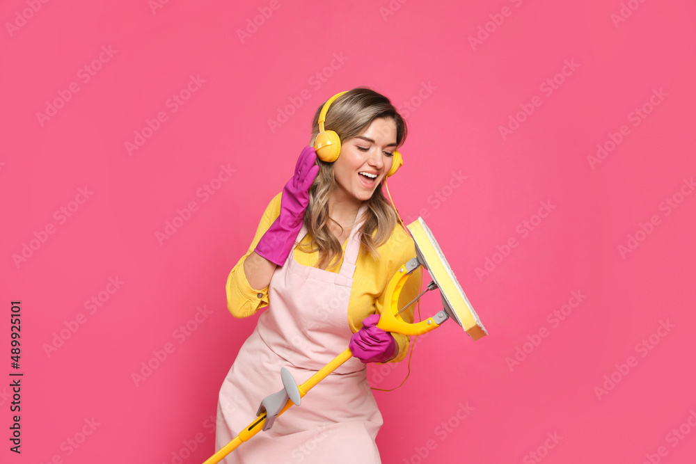 Beautiful young woman with headphones and mop singing on pink background Beautiful young woman with headphones and mop singing on pink background