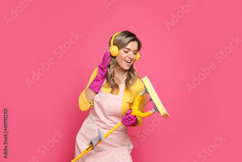 Beautiful young woman with headphones and mop singing on pink background © New Africa