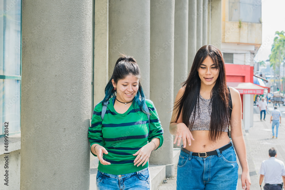 two beautiful latina girls (caucasian and brunette) walking down the street very cheerful while talking and discussing their dreams and future goals. two smiling women taking a stroll through the city two beautiful latina girls (caucasian and brunette) walking down the street very cheerful while talking and discussing their dreams and future goals. two smiling women taking a stroll through the city
