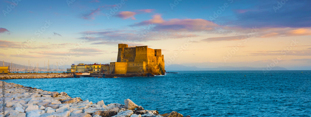 Naples, Italy. Castel dell'Ovo with breakwater rocks in the foreground and with a beautiful sunset sky. Banner Header.