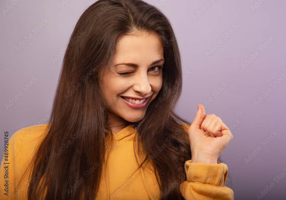 Relaxing thinking smiling woman give a wink one eye in fashion yellow hoodie looking happy on purple bright background with empty copy space. closeup Relaxing thinking smiling woman give a wink one eye in fashion yellow hoodie looking happy on purple bright background with empty copy space. closeup