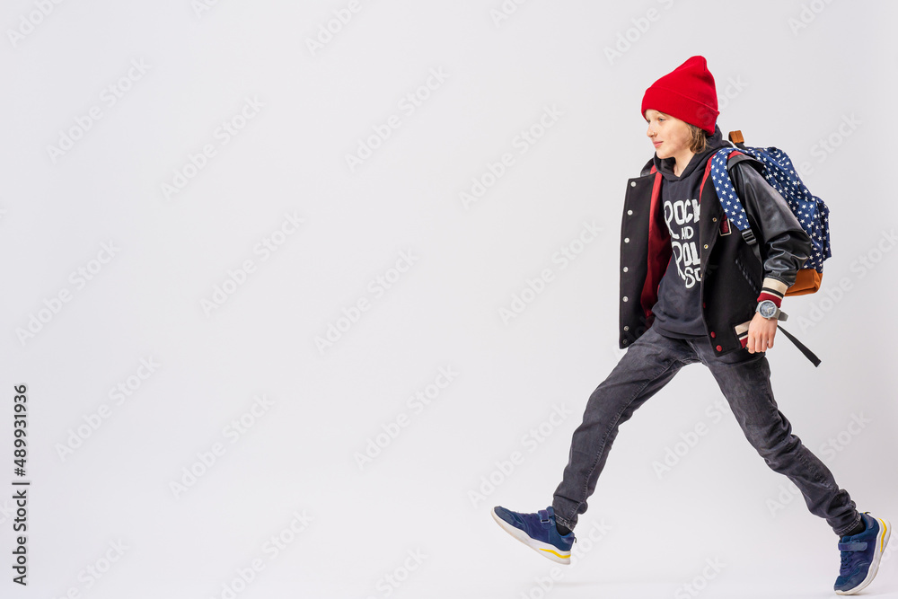 Portrait of teenage schoolboy in fashionable clothes with backpack on his shoulder, full-length, walking on white background. Adolescence. Advertising of teenage clothes and satchels. Copy space Portrait of teenage schoolboy in fashionable clothes with backpack on his shoulder, full-length, walking on white background. Adolescence. Advertising of teenage clothes and satchels. Copy space