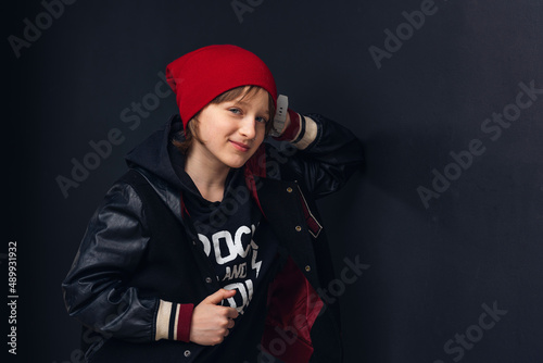 cute pre-teen boy with a nose piercing, in fashionable clothes stands near a black wall and looks into the camera. Adolescence. The concept of youth and clothing.