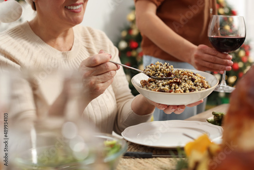 Woman with bowl of traditional Christmas kutia and her family at festive dinner, closeup. Slavic dish