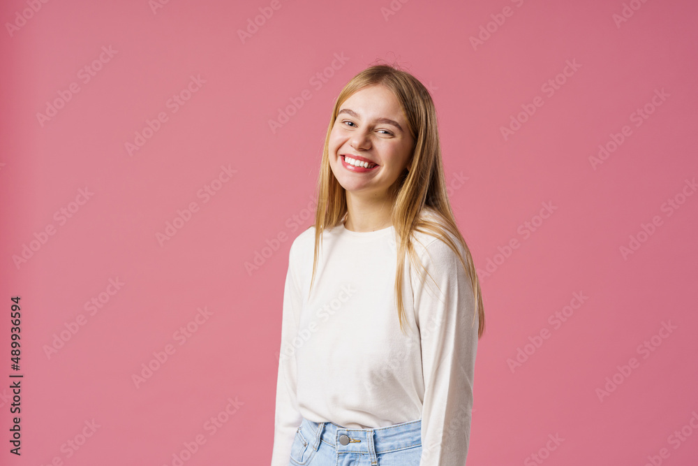 Portrait of a happy girl with long blonde hair, smiling and rejoicing. A teenager, emotionally excited with delight, looks into the camera, standing on a pink background in the studio Portrait of a happy girl with long blonde hair, smiling and rejoicing. A teenager, emotionally excited with delight, looks into the camera, standing on a pink background in the studio