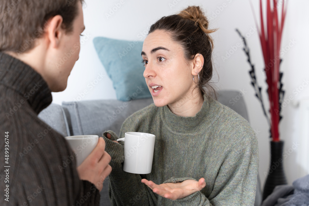 Young woman having conversation with friend and holding a cup of coffee Young woman having conversation with friend and holding a cup of coffee