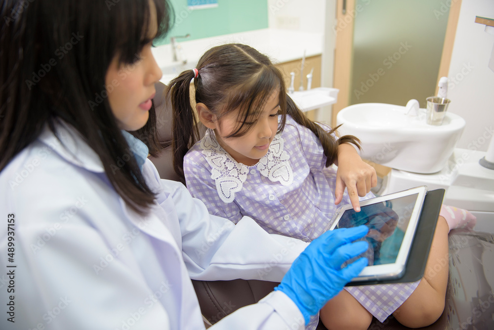 Female dentist explaining teeth x-ray to a little girl in dental clinic, teeth check-up and Healthy teeth concept Female dentist explaining teeth x-ray to a little girl in dental clinic, teeth check-up and Healthy teeth concept