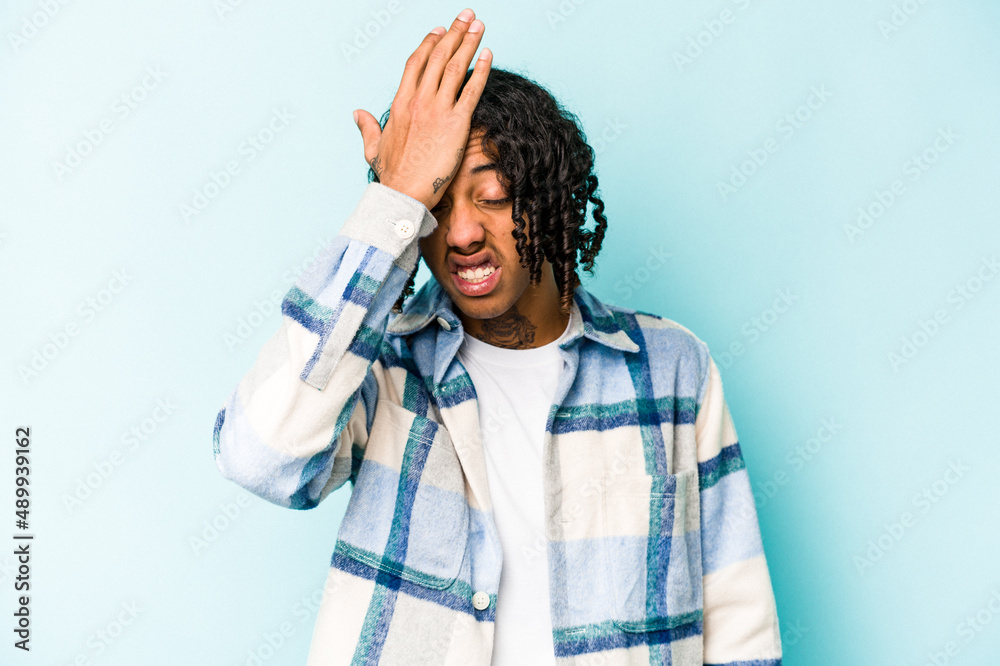 Young African American man isolated on blue background forgetting something, slapping forehead with palm and closing eyes. Young African American man isolated on blue background forgetting something, slapping forehead with palm and closing eyes.