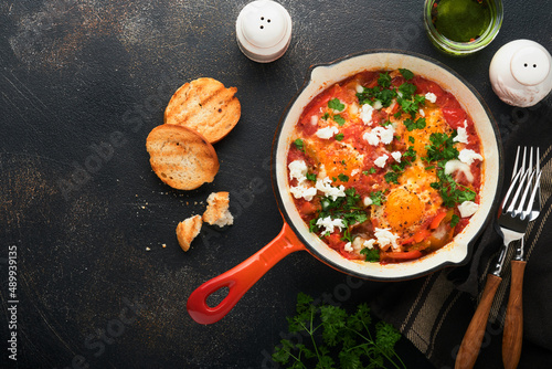 Shakshuka. Homemade fried eggs with vegetables in iron frying pan on old dark slate, stone or concrete background. Traditional cuisine of Israel. Late breakfast concept. Arabic cuisine. Top view.