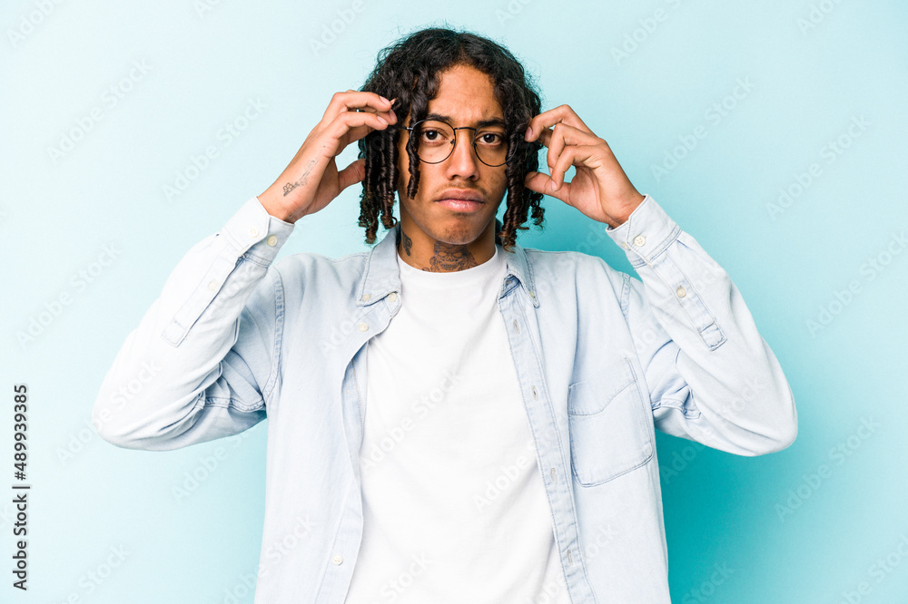 Young African American man isolated on blue background focused on a task, keeping forefingers pointing head. Young African American man isolated on blue background focused on a task, keeping forefingers pointing head.