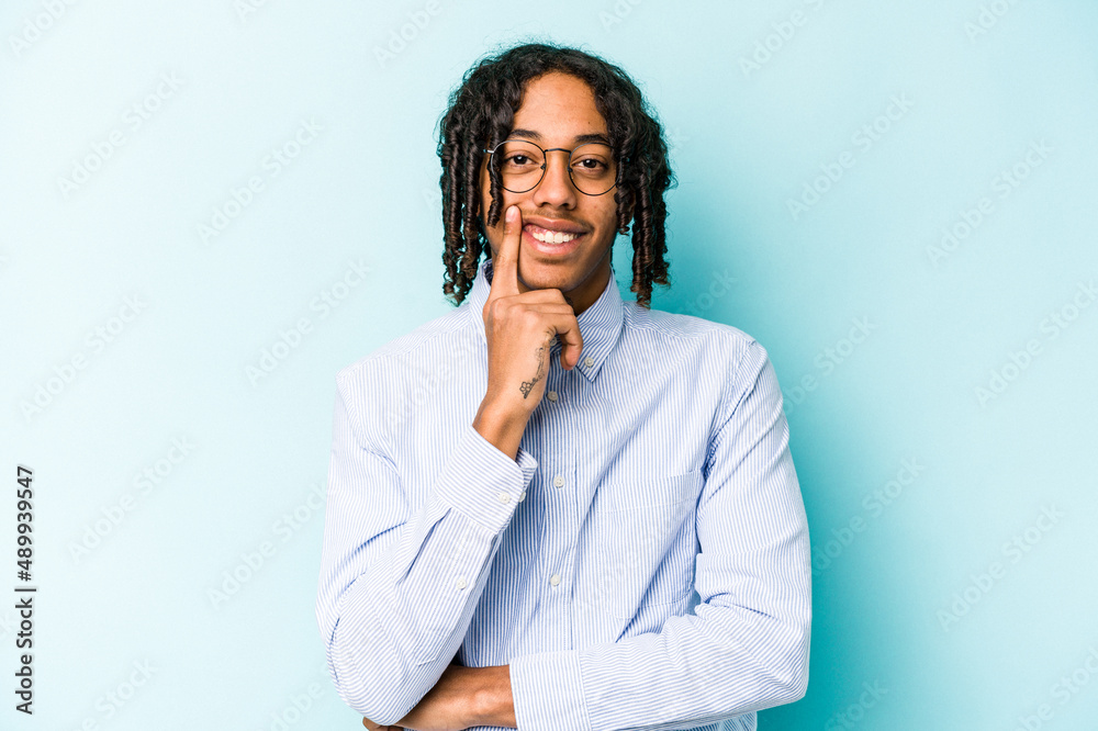 Young African American man isolated on blue background smiling happy and confident, touching chin with hand. Young African American man isolated on blue background smiling happy and confident, touching chin with hand.