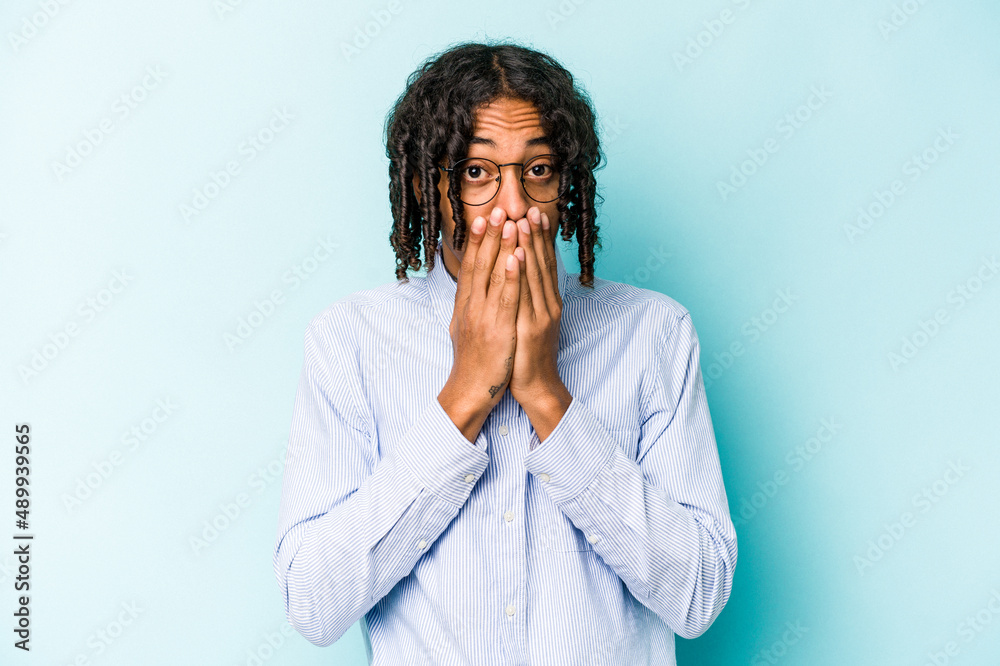 Young African American man isolated on blue background covering mouth with hands looking worried.