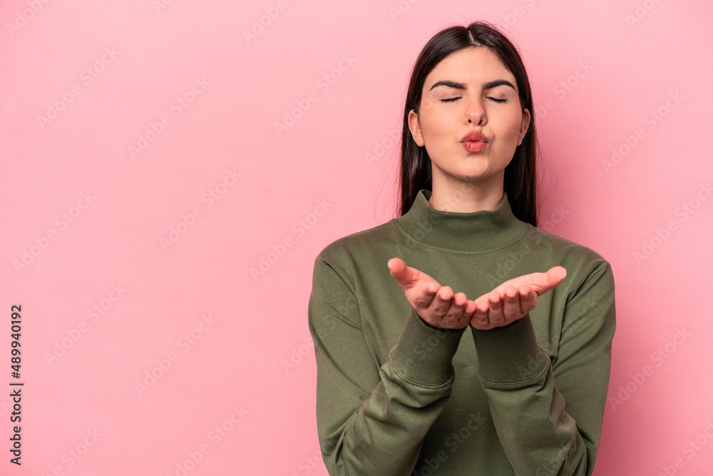 Young caucasian woman isolated on pink background folding lips and holding palms to send air kiss. Young caucasian woman isolated on pink background folding lips and holding palms to send air kiss.