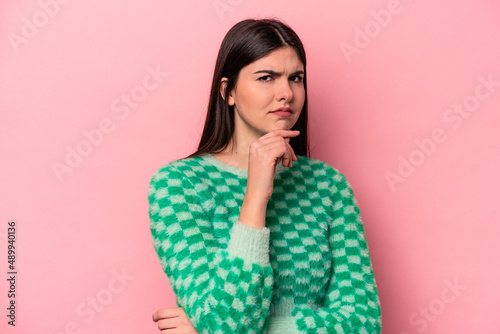Young caucasian woman isolated on pink background suspicious, uncertain, examining you.