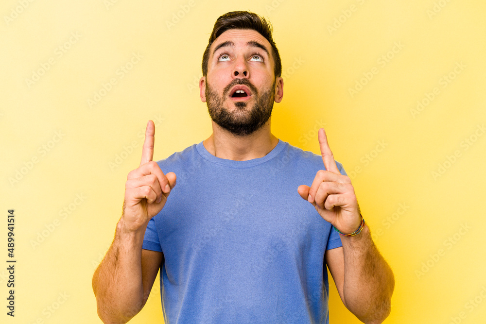Young caucasian man isolated on yellow background pointing upside with opened mouth. Young caucasian man isolated on yellow background pointing upside with opened mouth.