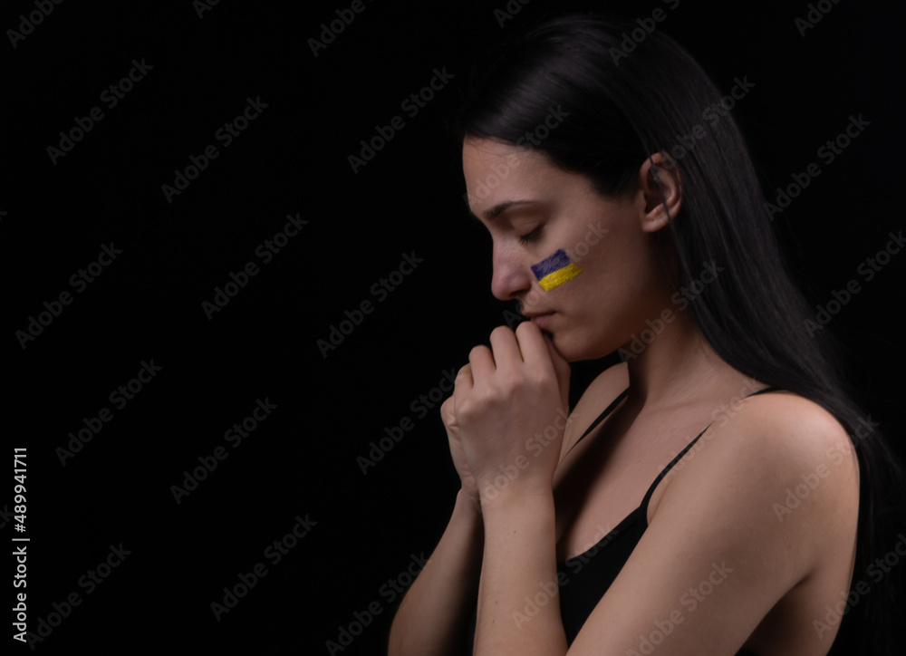 Portrait of serious ukrainian woman with blue and yellow ukrainian flag on her cheek.The symbol of the inviolability of the Ukrainian people. Dark background. Space for your text Portrait of serious ukrainian woman with blue and yellow ukrainian flag on her cheek.The symbol of the inviolability of the Ukrainian people. Dark background. Space for your text