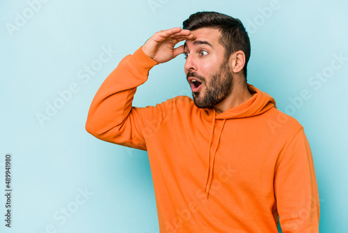 Obraz na płótnie Young caucasian man isolated on blue background looking far away keeping hand on forehead