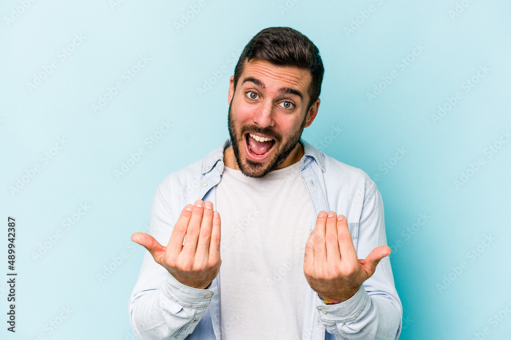 Young caucasian man isolated on blue background pointing with finger at you as if inviting come closer.
