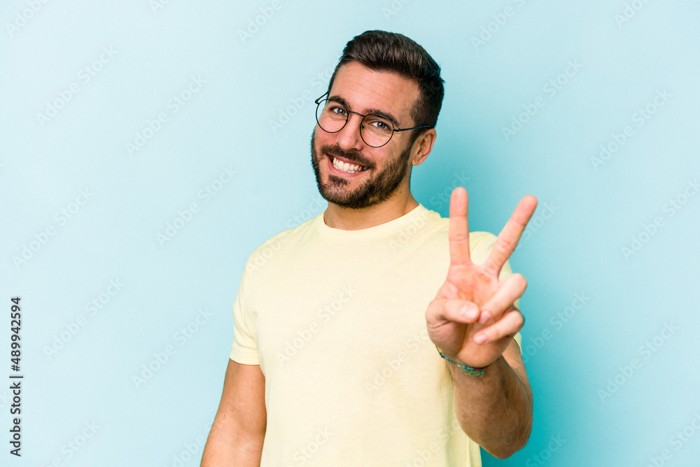 Young caucasian man isolated on blue background joyful and carefree showing a peace symbol with fingers. Young caucasian man isolated on blue background joyful and carefree showing a peace symbol with fingers.