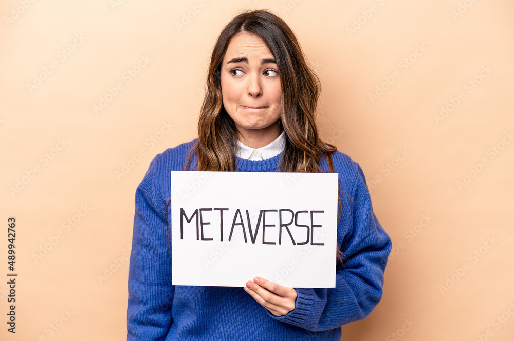 Young caucasian woman holding a metaverse placard isolated on beige background confused, feels doubtful and unsure. Young caucasian woman holding a metaverse placard isolated on beige background confused, feels doubtful and unsure.