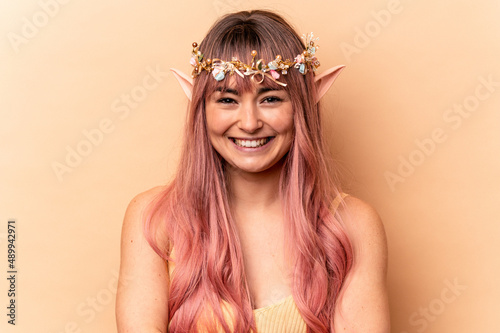 Young elf woman with pink hair isolated on beige background laughing and having fun.