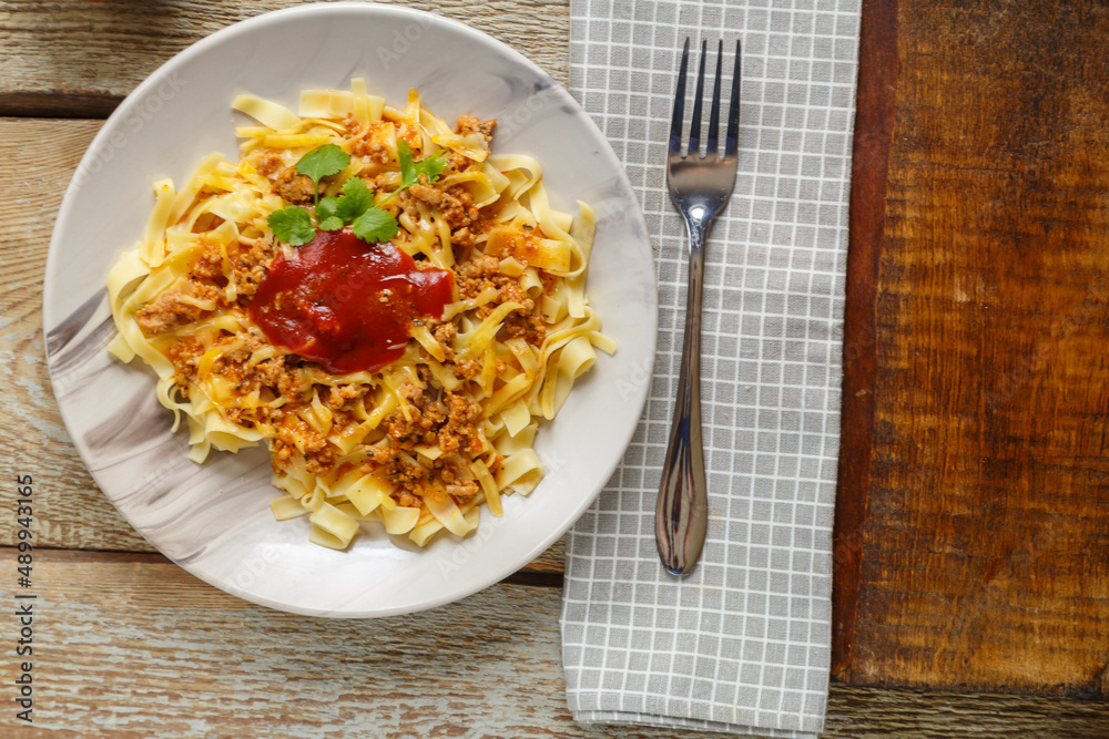 Pasta bolognese garnished with herbs and cheese in a plate on a wooden table next to a fork and a napkin. Pasta bolognese garnished with herbs and cheese in a plate on a wooden table next to a fork and a napkin.