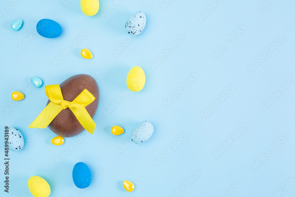 Broken and whole chocolate Easter eggs, multicolored sweets on blue background. Concept of celebrating Easter, Easter decorations, search for sweets for Easter Bunny. Flat lay, top view. Copy Space.