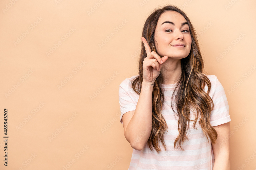 Fototapeta premium Young caucasian woman isolated on beige background showing number one with finger.
