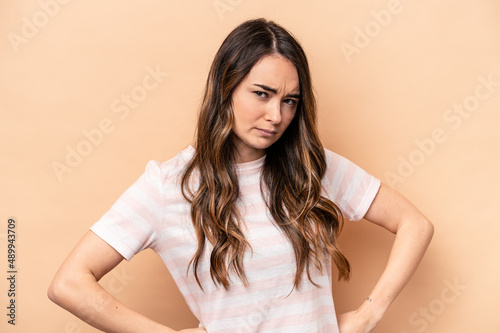 Young caucasian woman isolated on beige background frowning face in displeasure, keeps arms folded.