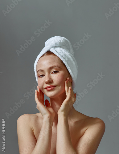 Pretty young girl in towel with bare shoulders, touches perfect smooth skin, massaging face. Natural beauty, self care