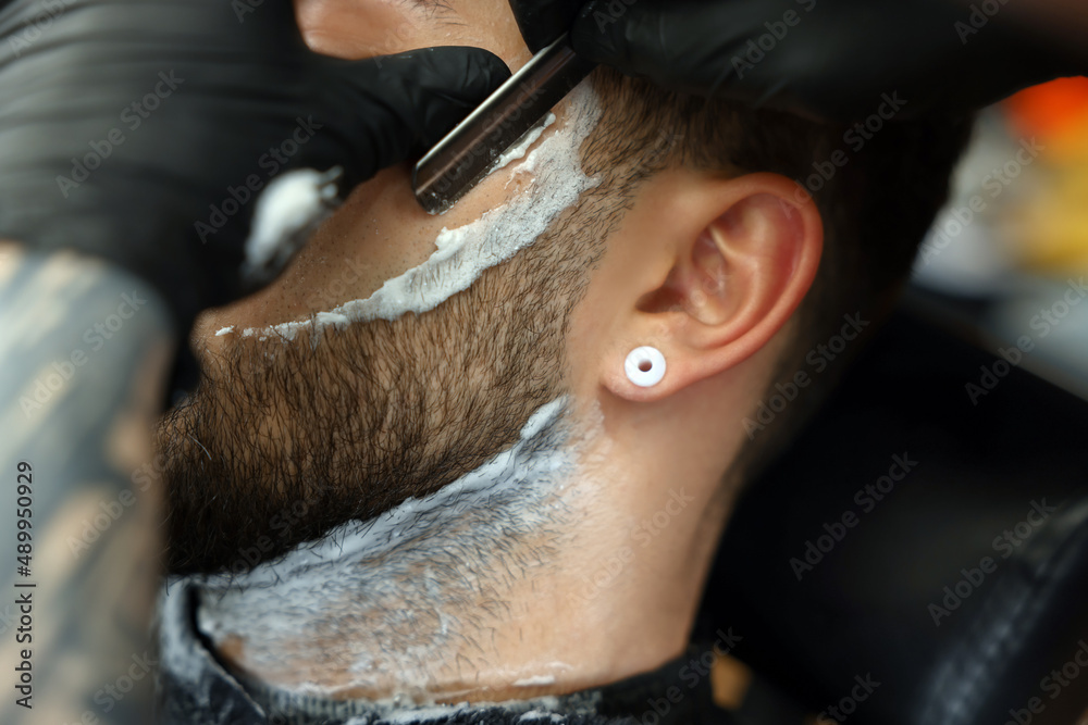 Obraz premium Professional hairdresser working with bearded client in barbershop, closeup