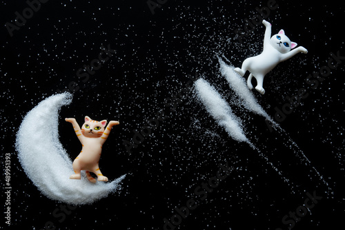 Funny toy ginger cat stands on white powder crescent, next to stars and asteroid trails. Black background. Concept infinity space, predictions of the future and fortune-telling on moon cat photo