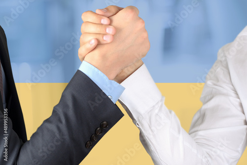 Business patners shaking hands in reconcilation. Ukraine flag is behind.