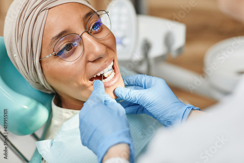 Close up of young Middle-Eastern woman in dental chair with mouth open during examination in clinic
