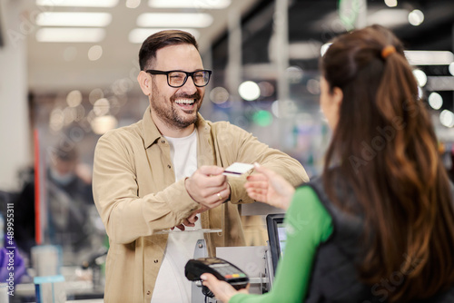 A happy man giving credit card to cashier in supermarket and paying check.