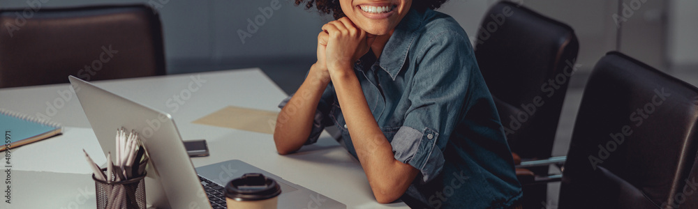 Positive pretty woman working with laptop while sitting at desk and looking away in the office