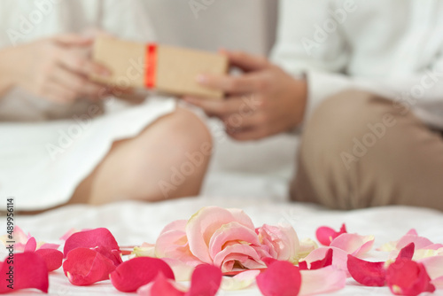 Rose petals in the foreground. The couple in the background give gifts.